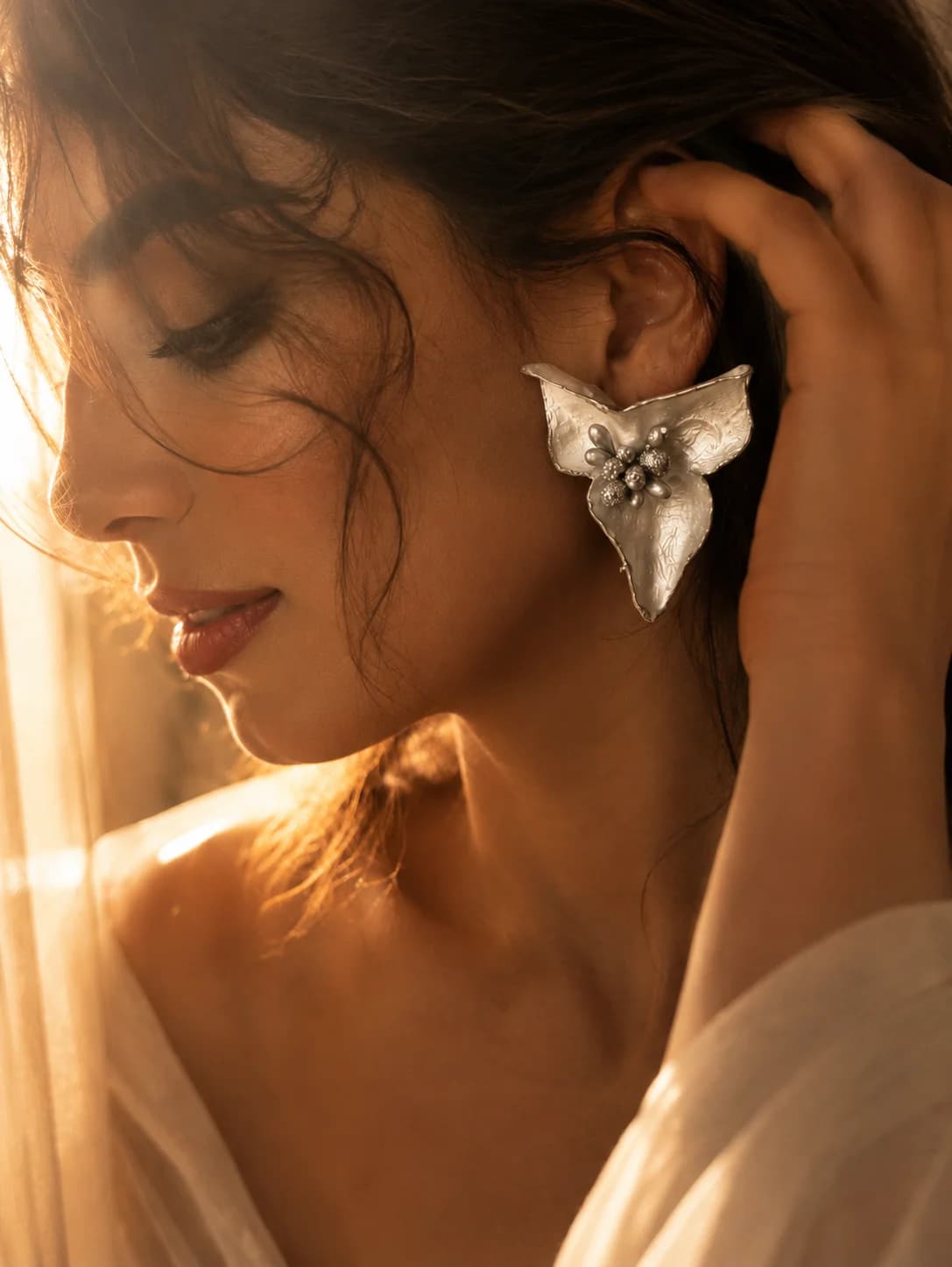 Silver-toned paper leaf earring in warm light — handmade wearable art by Sara Idee